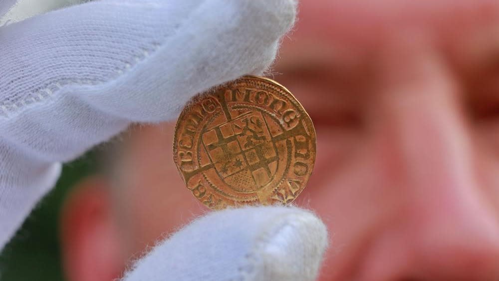  A person wearing gloves holds a gold coin. 