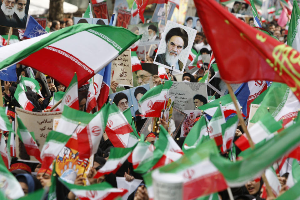 FILE - In this Nov. 4, 2009 file photograph, waving flags, Iranian school girls attend an annual demonstration in front of the former U.S. Embassy in Tehran, Iran, commemorating the 30th anniversary of the seizure of the U.S. Embassy by militant students. The poster at top center shows Iran's late revolutionary founder Ayatollah Ruhollah Khomeini. Iran's 1979 Islamic Revolution initially inspired both Islamic militants and Islamists across the Mideast. They saw the revolution as the starting gun in a competition to push out the strongman Arab nationalism that had taken hold across the Middle East. However, analysts say Iran's push to back militants in the wider Mideast and Saudi Arabia's efforts to mobilize the Sunni world against the Shiite power would turn many away. (AP Photo/Vahid Salemi, File)