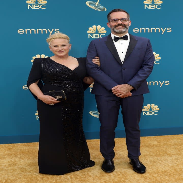 Patricia Arquette in a black gown and holding a purse with a man in a tux