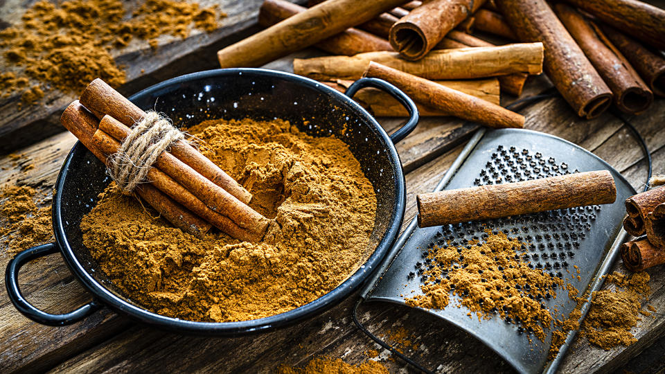 High angle view of a rustic wooden table with cinnamon sticks and ground cinnamon. A small grater is in a container filled with ground cinnamon. Predominant color is brown. High resolution 42Mp studio digital capture taken with SONY A7rII and Zeiss Batis 40mm F2.0 CF lens (fcafotodigital / Getty Images stock)