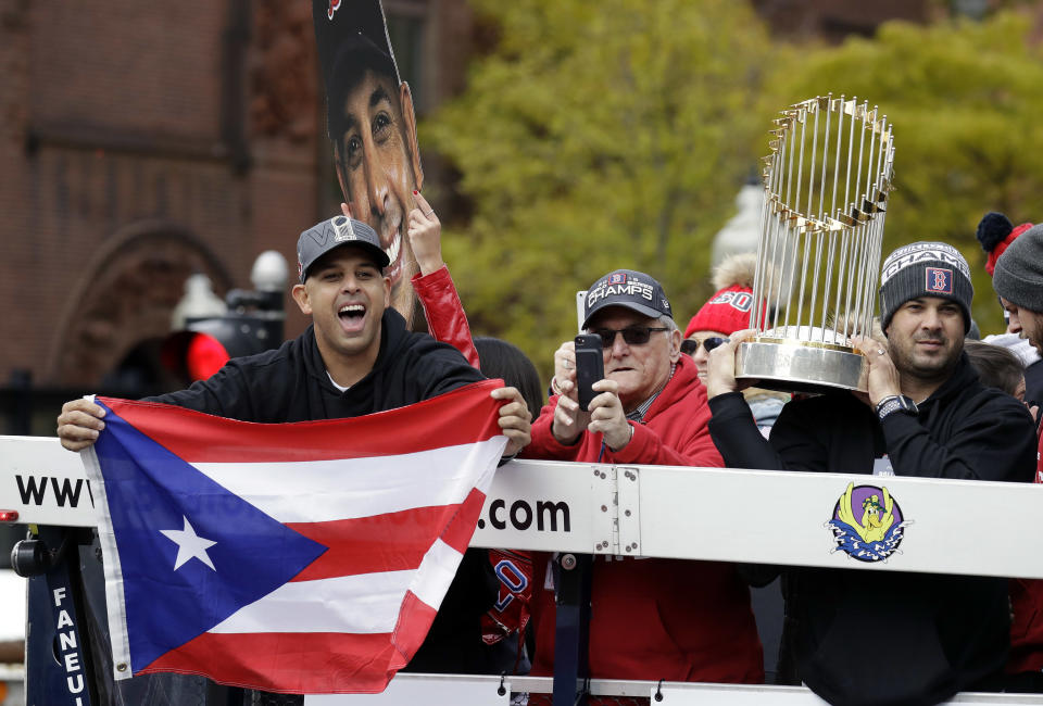 Boston Red Sox manager Alex Cora waves the flag of Puerto Rico as coach Ramon Vazquez holds the championship trophy during the World Series parade. (AP)