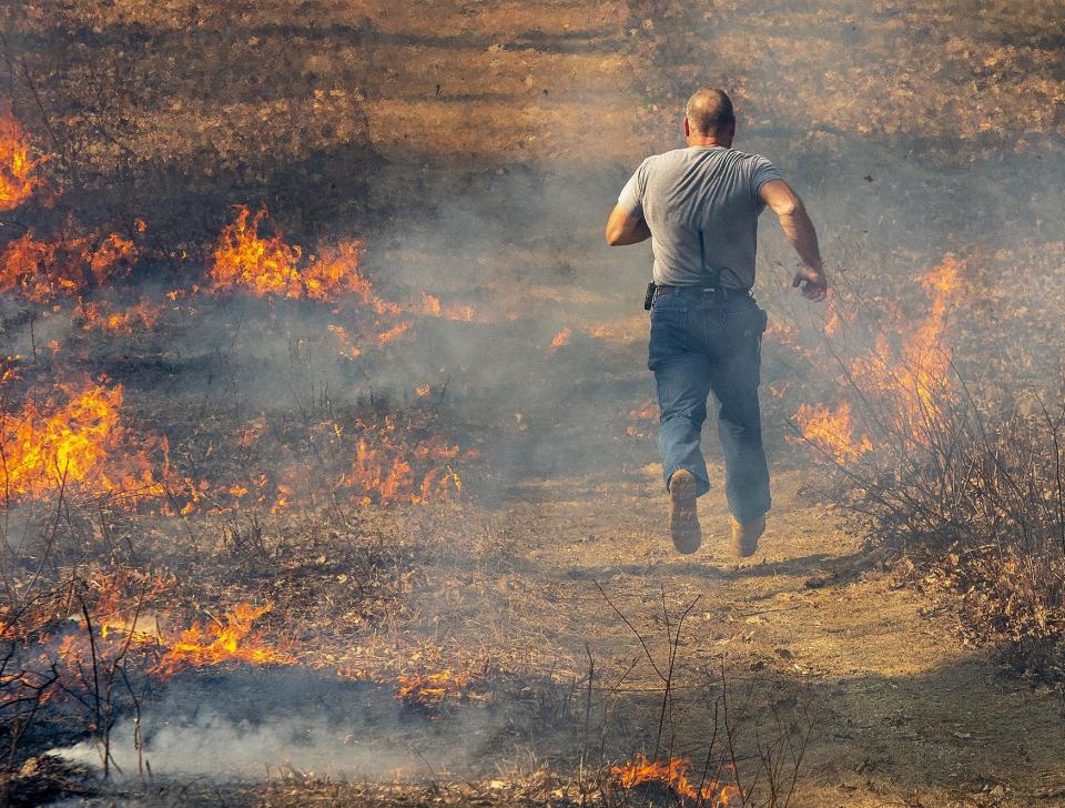 In 2020, Assistant Millbury Fire Chief Brian Gasco runs to save a hose from moving flames during a brush fire in Sutton, Massachusetts.