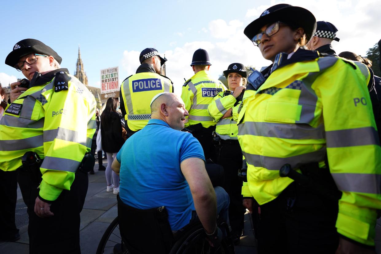 Police officers with a Jewish man in a wheelchair with protesters behind during a March for Palestine in London (PA)