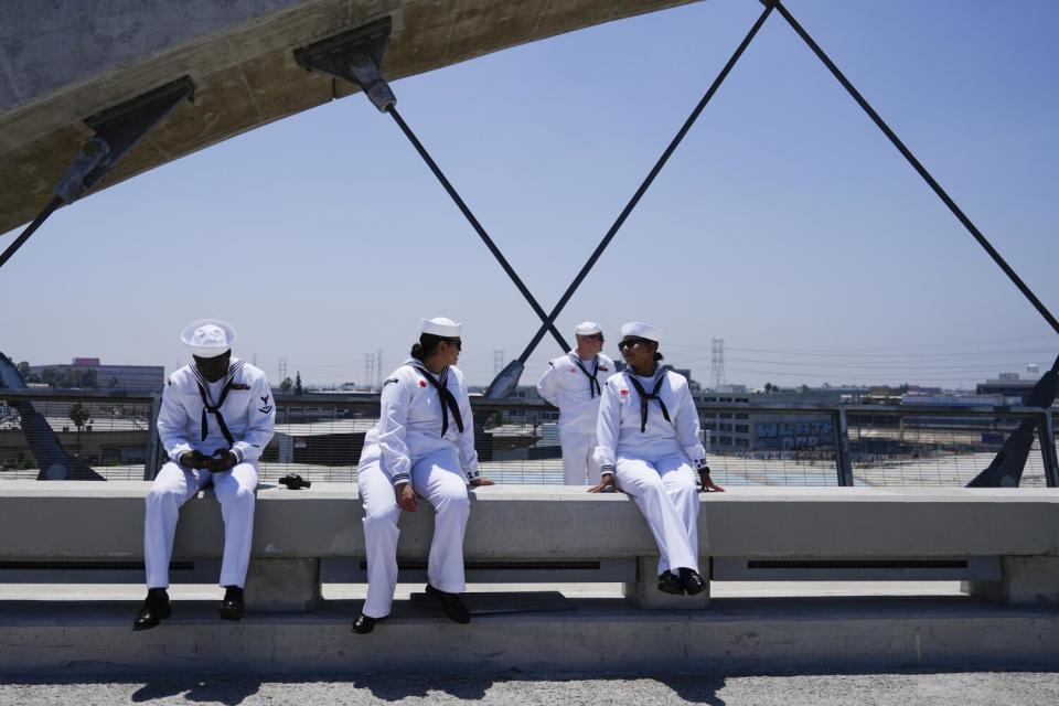 A few people in white uniforms sit on a concrete barrier.