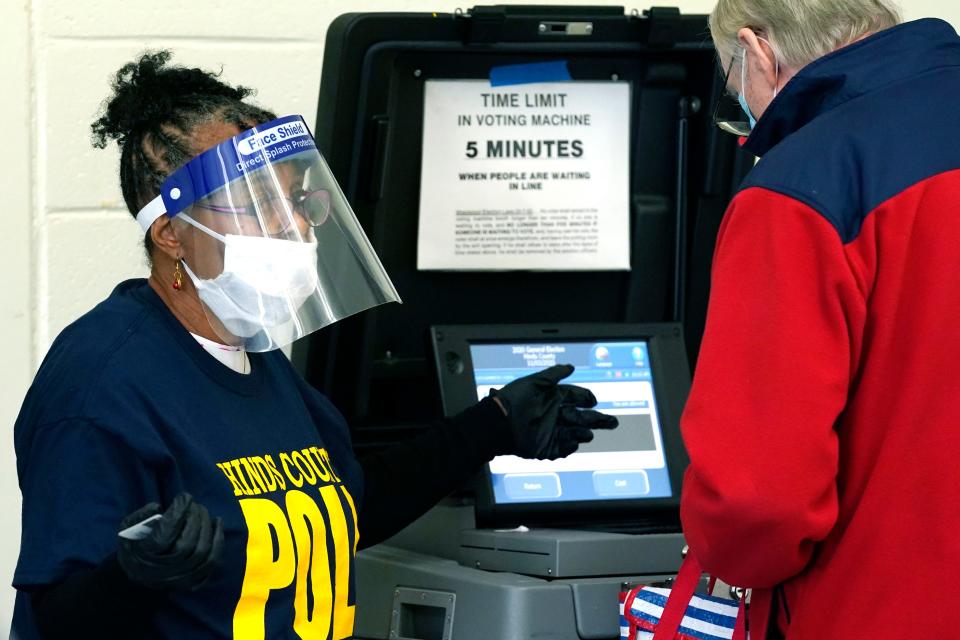 Poll worker Vivian Bibens is decked out in her personal protective equipment as she explains the purpose of the ballot scanner to a voter on Election Day in Jackson, Miss., on Nov. 3, 2020.