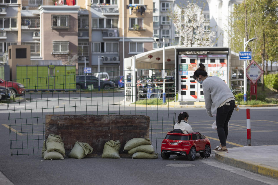 A mother watches as her daughter play in a toy car next to a barrier set up at the gate of a residential community under lock down in Shanghai, China, Tuesday, March 29, 2022. A two-phase lockdown of Shanghai's 26 million people is testing the limits of China's hard-line "zero-COVID" strategy, which is shaking markets far beyond the country's borders. (AP Photo)