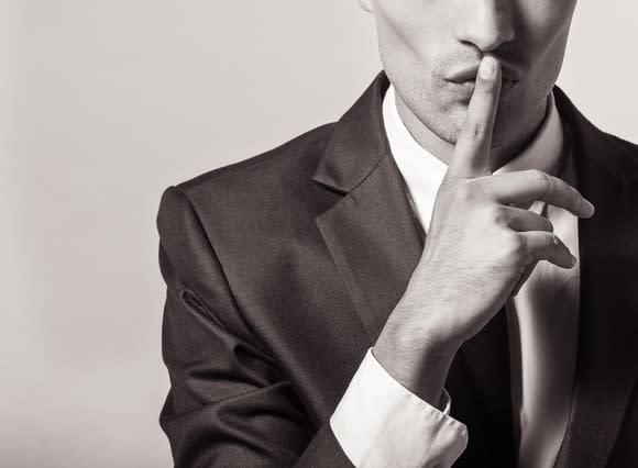 A man holding a finger to his lips to make a shushing sound.