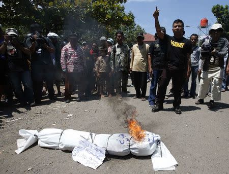 People watch as a small group of anti-drug activists try to burn an effigy during a protest near the ferry crossing for the prison island of Nusakambangan, where upcoming executions are expected, in Cilacap, Central Java March 6, 2015. REUTERS/Darren Whiteside