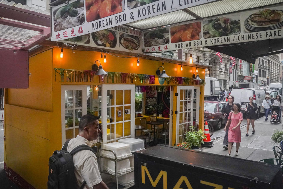 A restaurant's pandemic-era outdoor dining shed, left, sits on street parking spaces in mid-town Manhattan, Tuesday Aug. 8, 2023, in New York. New York City's roadway dining sheds, a pandemic innovation, are coming under new rules for design and seasonality. (AP Photo/Bebeto Matthews)