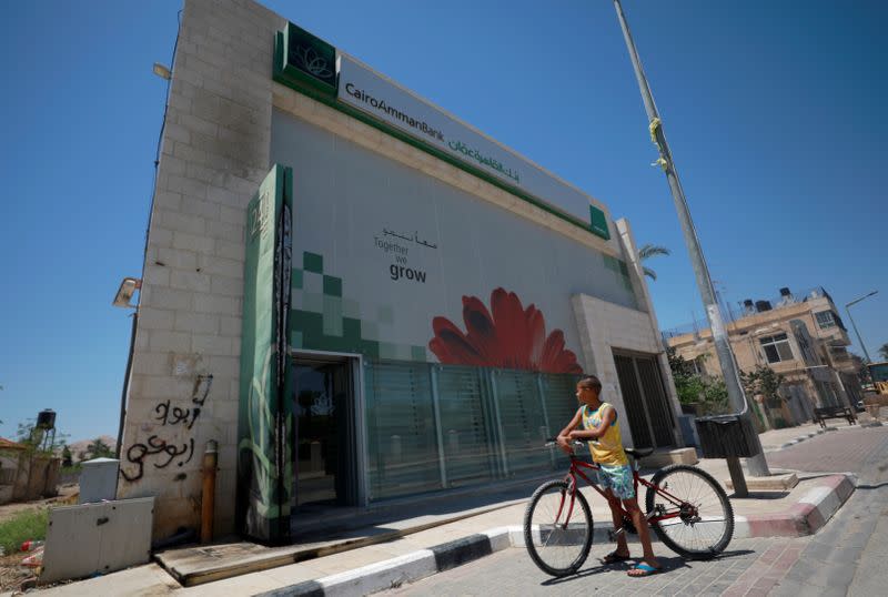 A Palestinian boy with a bicycle looks at a burnt part of the exterior of the Cairo Amman Bank, in Jericho in the Israeli-occupied West Bank