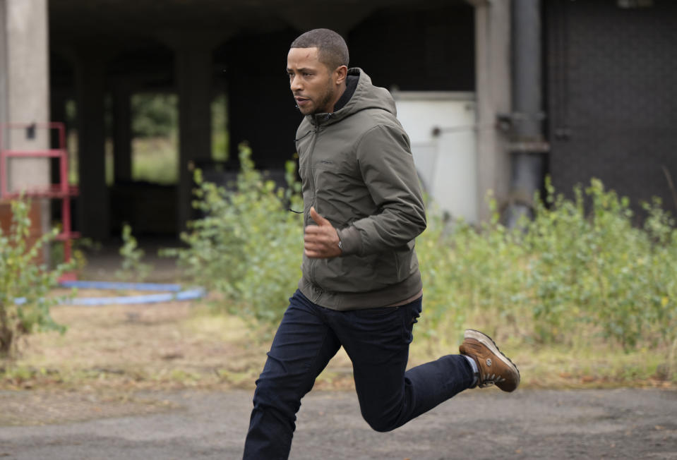 DS Tyrone Clarke (Ukweli Roach) running in a grassy industrial area