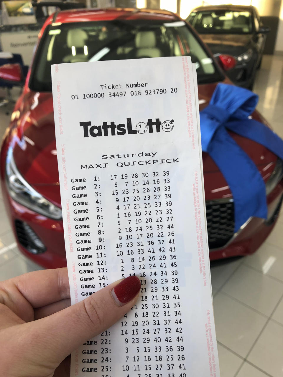 A woman holds a Saturday lotto ticket in front of a brand new car. 