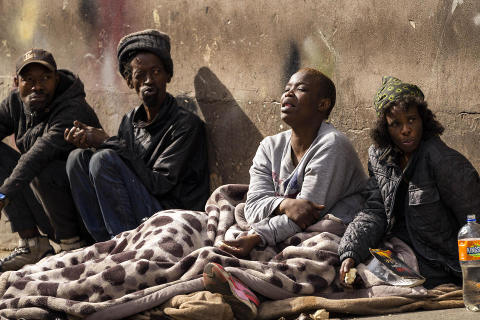 Homeless people sit near the scene of one of South Africa's deadliest inner-city fires in Johannesburg, South Africa, Friday, Sept. 1, 2023. Emergency services teams have left the scene of one of South Africa's deadliest inner-city fires as pathologists faced the grisly task Friday of identifying dozens of charred bodies and some separate body parts that had been transported to several mortuaries across the city of Johannesburg. (AP Photo/Jerome Delay)
