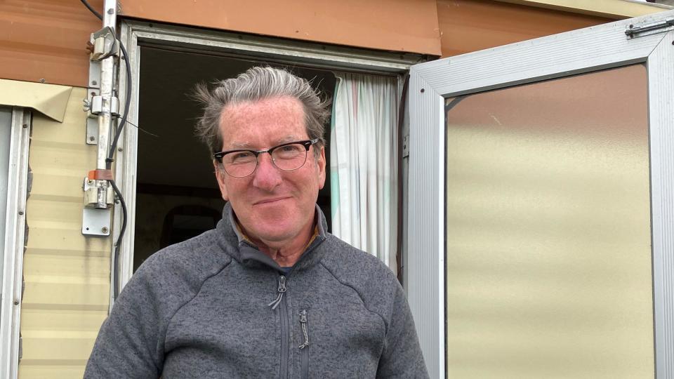 Man wearing glasses and a grey jumper standing in front of his caravan 