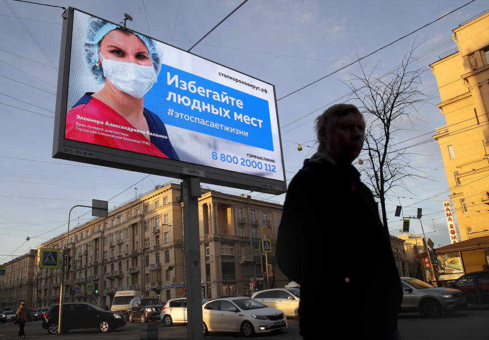 A man walks past an electronic billboard showing a doctor wearing a medical mask with the words reading âAvoid crowded places, it will save a life" in a street in St.Petersburg, Russia on March 25, 2020. (Dmitri Lovetsky/AP)