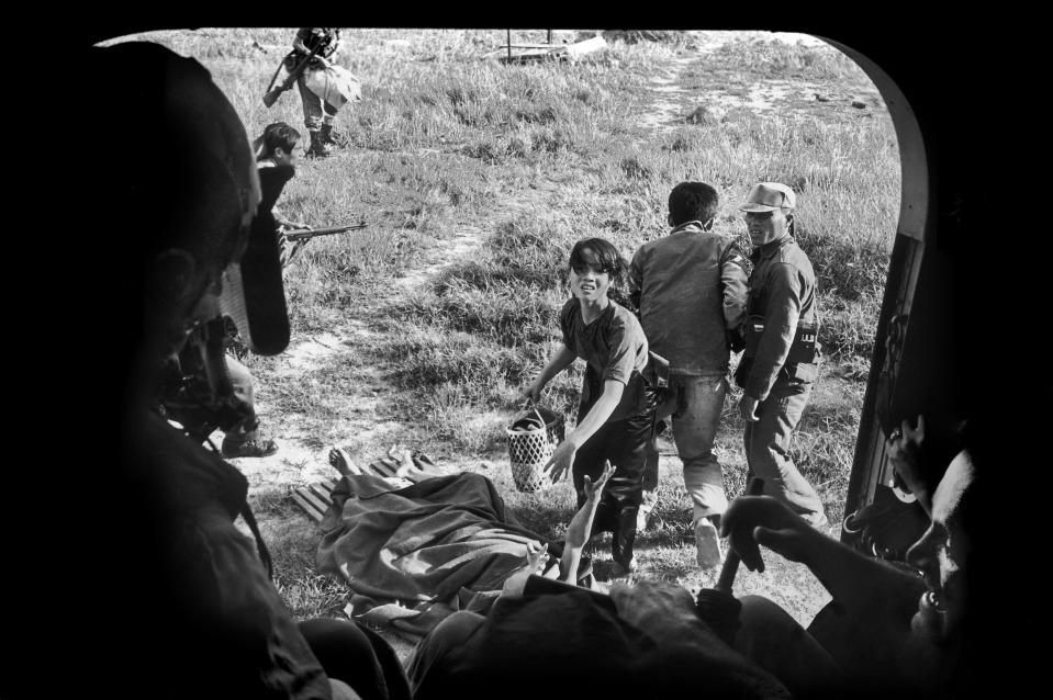 A Vietnamese woman pleads with U.S. soldiers to allow her and her wounded husband, on the ground with his arm outstretched, onto the evacuation helicopter so they can escape a Viet Cong attack in Ba Gia, July 1965. The couple were left behind. (AP Photo/Eddie Adams)
