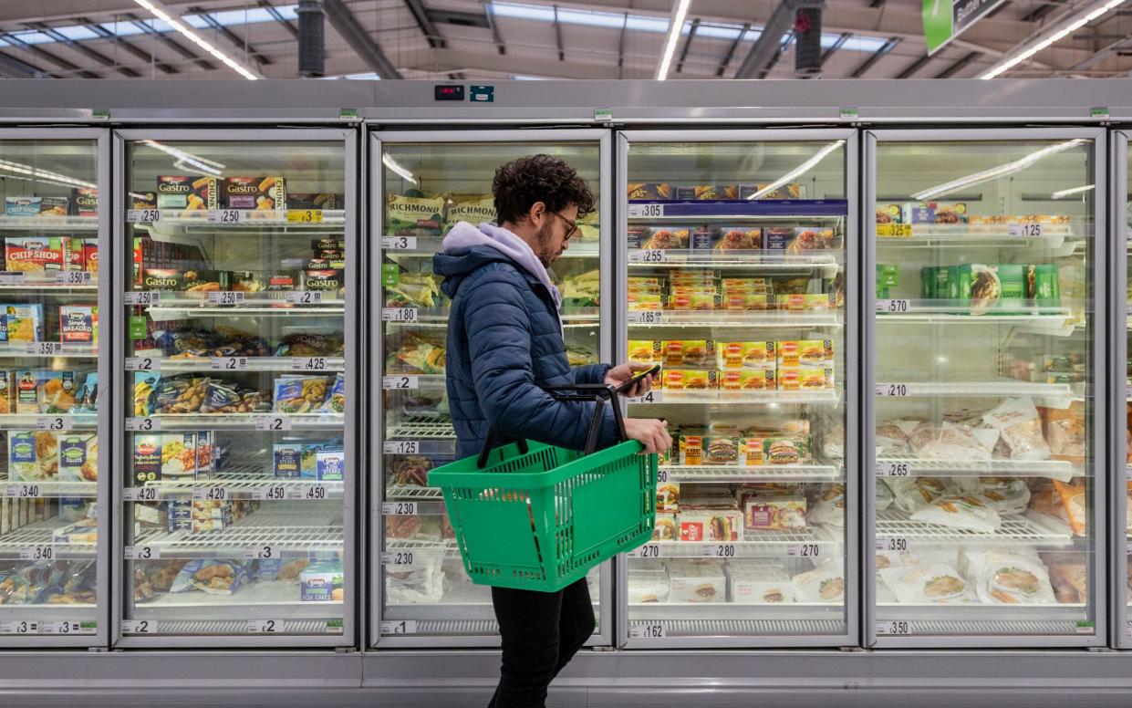 A man reads a shopping list in front of a freezer full of forzen products