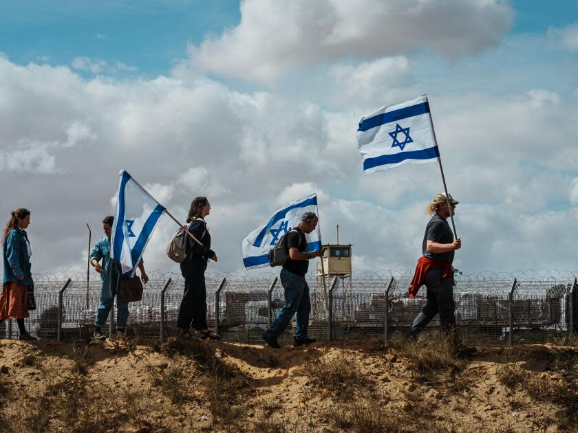 A small group, including three people holding Israeli flags, walking near a high-security fence