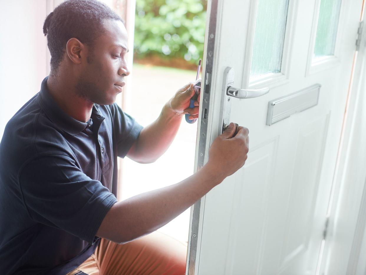 A young locksmith changing the lock on a residential front door.