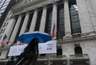 A woman with an umbrella passes the New York Stock Exchange, Monday, Oct. 26, 2020. U.S. stocks are drifting Tuesday, Oct. 27, 2020, as momentum slows a day after Wall Street slumped to its worst loss in a month on worries about rising virus counts and Washington’s inability to deliver more aid to the economy. The (AP Photo/Mark Lennihan)