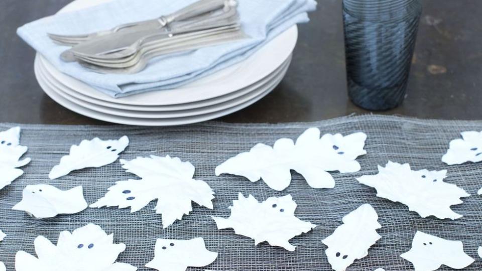 assortment of leaves painted white with two black eyes to look like ghosts displayed on table for halloween