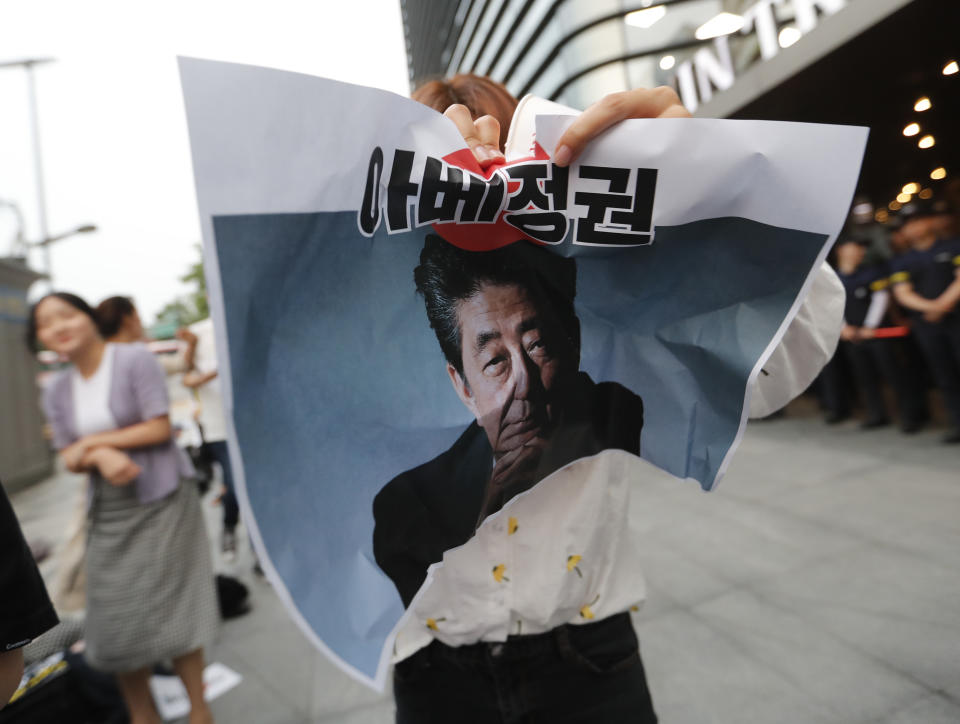 In this Thursday, July 18, 2019, photo, a protester tries to tear a paper showing an image of Japanese Prime Minister Shinzo Abe during a rally denouncing the Japanese government's decision on their exports to South Korea in front of the Japanese embassy in Seoul, South Korea. South Korean police on Friday, July 19, say a man has set himself on fire in front of the Japanese Embassy in Seoul amid rising trade disputes between Seoul and Tokyo. The signs read "Abe's government." (AP Photo/Ahn Young-joon)