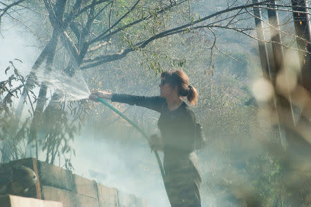 Elizabeth Rawjee sprays water from a garden hose onto hotspots left by the Skirball fire in her backyard on the west side of Los Angeles, California, U.S., December 6, 2017. REUTERS/Andrew Cullen