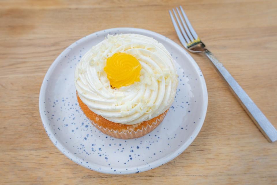 Small cake with swirl of white frosting and yellow swirl in the center on a plate next to a fork