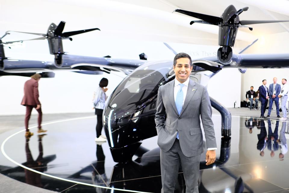 Nikhil Goel of Archer smiling wearing a grey suit and cyan tie stood in front of the Midnight eVTOL at the Dubai Air Show