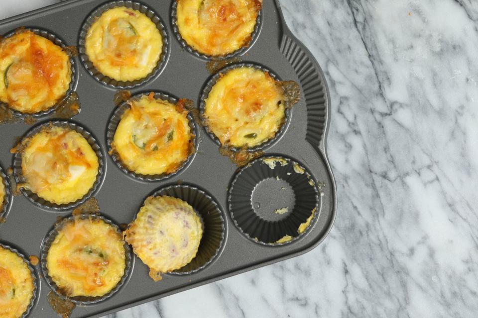 an overhead close up horizontal photograph of a baking pan with freshly made egg bites, it appears the chef has already sampled one of them