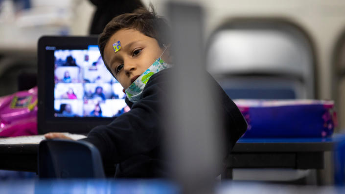 Un enfant est assis à une table devant un ordinateur, sur lequel un cours en ligne est visible.