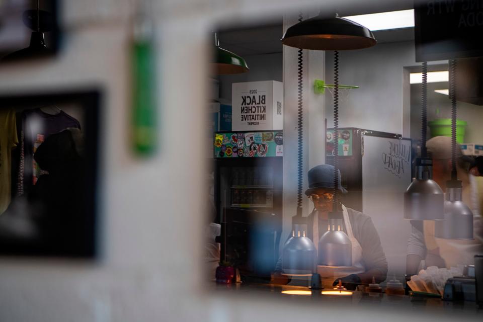 Chef Ashleigh Shanti is reflected in one of the framed historic photographs of Asheville’s Black community by Andrea Clark hanging on the wall at Good Hot Fish, January 19, 2024.