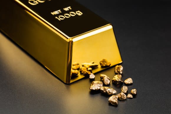 A polished bar of gold bullion next to smaller gold fragments.