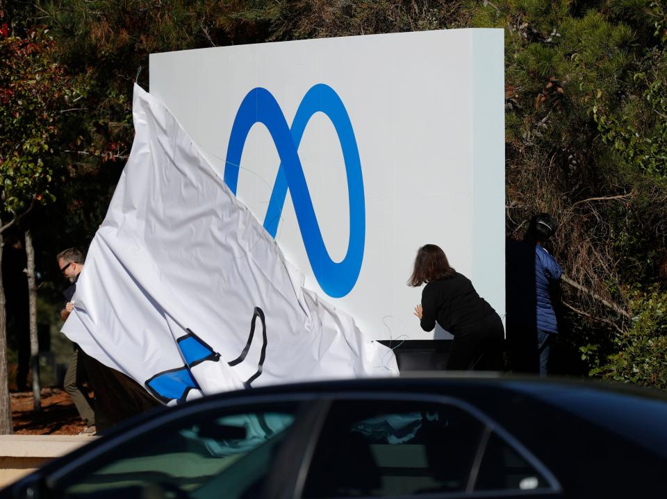 Workers in front of Facebook headquarters pull off cover of the old "thumbs up" sign to reveal the new Meta logo