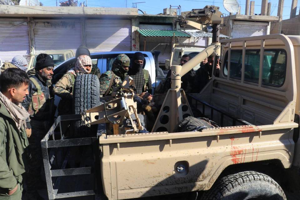 This photo provided by the Kurdish-led Syrian Democratic Forces shows fighters from the Kurdish-led Syrian Democratic Forces gathered around a body of an Islamic State group gunman who was killed after they attacked Gweiran Prison, in Hassakeh, northeast Syria, Friday, Jan. 21, 2022. IS attacks have been on the rise in recent months in both Iraq and neighboring Syria, where the group once set up a self-styled Islamic caliphate before being defeated by an international coalition. (Kurdish-led Syrian Democratic Forces via AP)