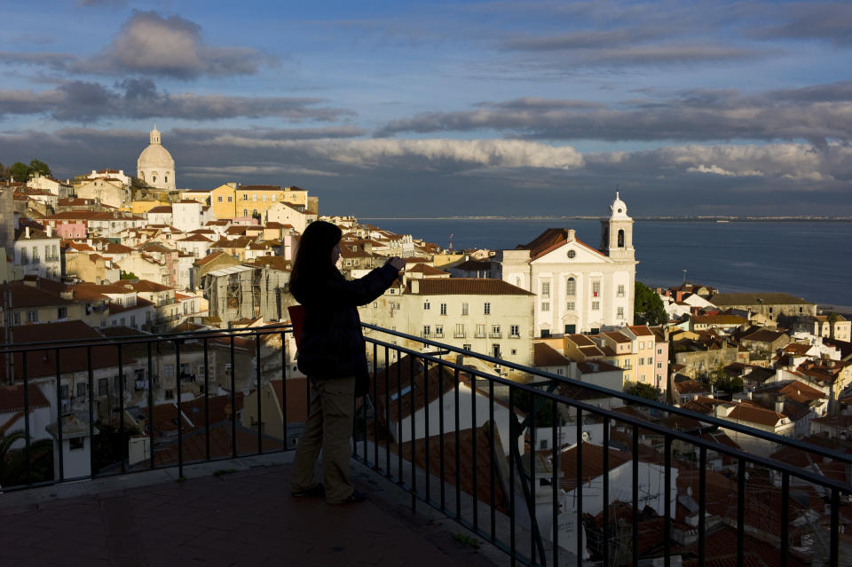 In this photo taken Dec. 18 2012, a tourist takes photos from a viewpoint overlooking Lisbon's Alfama neighborhood and the Tagus river. The Alfama quarter is distinguished by its narrow, cobbled streets on the hillside below Lisbon castle, where archaeologists have found traces of occupation dating from the seventh century B.C. (AP Photo/Armando Franca)