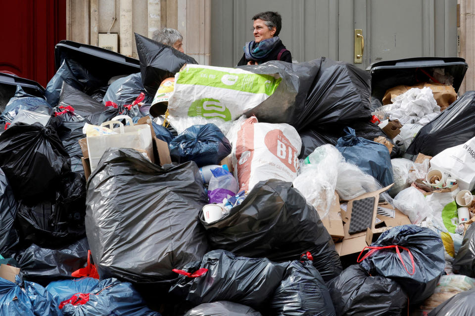 Women stand next to overflowing trash bins in Paris, on March 17, 2023. 