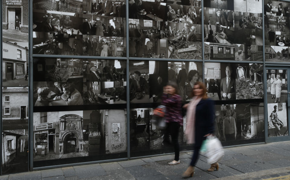 Two women walk past a montage of photographs showing past life in the city of Belfast, Northern Ireland, Friday, March 24, 2017. Almost 20 years on from the Good Friday peace accord, which brought about the end of Northern Ireland's sectarian conflict, the city of Belfast has changed dramatically. (AP Photo/Alastair Grant)