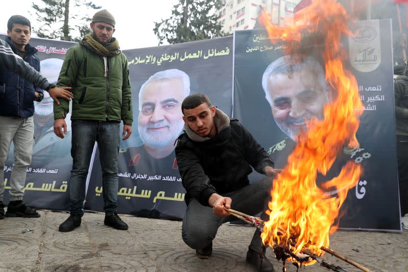 A Palestinian man burns representations of U.S. flag and Israeli flag in front of posters of Iranian Major-General Qassem Soleimani during a protest in Gaza