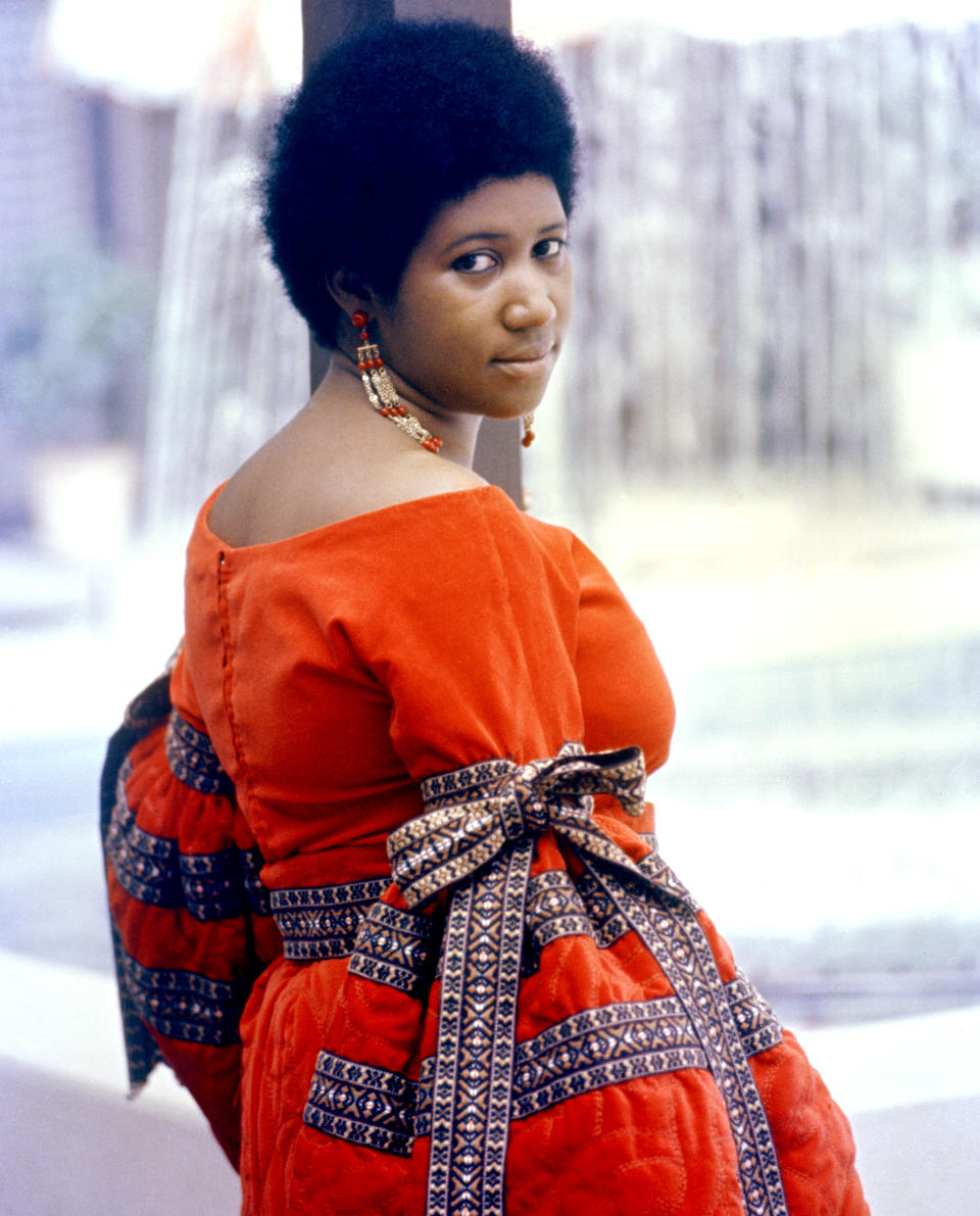 <p>Aretha Franklin wears a vibrant orange off-the-shoulder dress, matching bead earrings, and an Afro. (Photo: Getty Images) </p>