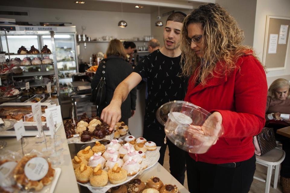 In this Thursday, Dec. 15, 2016 photo, a bakery employee helps customer choose doughnuts in Bnei Brak, Israel. Israelis are finding new advice hard to swallow: in the name of proper nutrition, their health minister has gone on the warpath against the beloved Hanukkah tradition of gorging on sugar-laden, deep-fried, jam-filled doughnuts. Yaakov Litzman _ the bearded, black-coated chief of a powerful ultra-Orthodox political party _ considers himself a guardian of Jewish traditions. But he also wears another hat, as a health conscious official on a crusade to stamp out junk food and child obesity. (AP Photo/Dan Balilty)