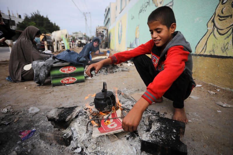 A Palestinian boy makes tea over a fire while women make unleavened bread on an open fire at a shelter in Rafah in the southern Gaza Strip on Friday. Photo by Ismael Mohamad/UPI