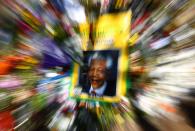 A poster depicting a photo of former South African President Nelson Mandela is seen among flowers outside of Mandela's house in Johannesburg December 15, 2013. South Africa buries Nelson Mandela on Sunday, closing one momentous chapter in its tortured history and opening another in which the multi-racial democracy he founded will have to discover if it can thrive without its central pillar. REUTERS/Yves Herman (SOUTH AFRICA - Tags: OBITUARY POLITICS)