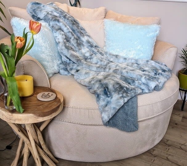 A cozy room with a plush sofa adorned with a faux fur throw and soft pillows, next to a wooden side table with a tulip vase