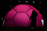 A woman wearing a traditional Qatari dress uses a cell phone to capture images in front of a soccer ball lit up in the colors of the Qatar flag during the FIFA fan festival at the World Cup soccer tournament in Doha, Qatar, Tuesday, Nov. 22, 2022. (AP Photo/Julio Cortez)