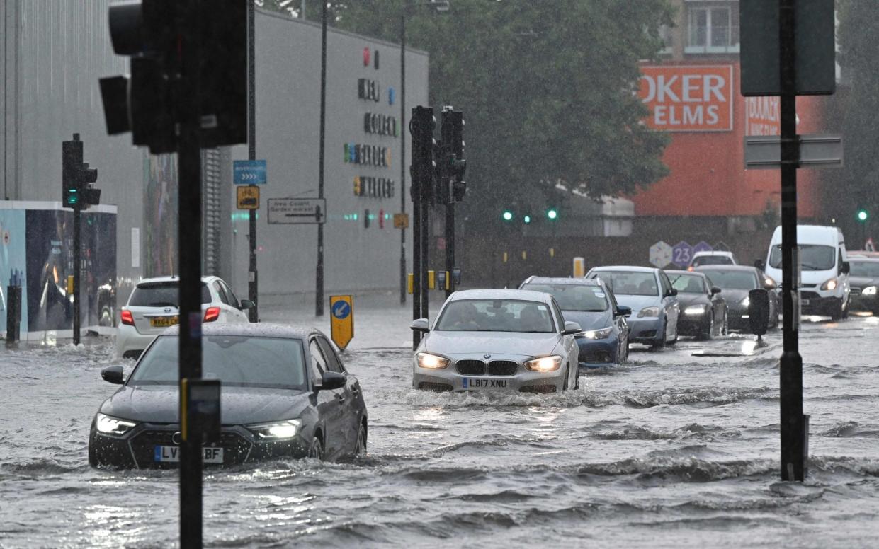 Cars drive through deep water on a flooded road in The Nine Elms, London - AFP