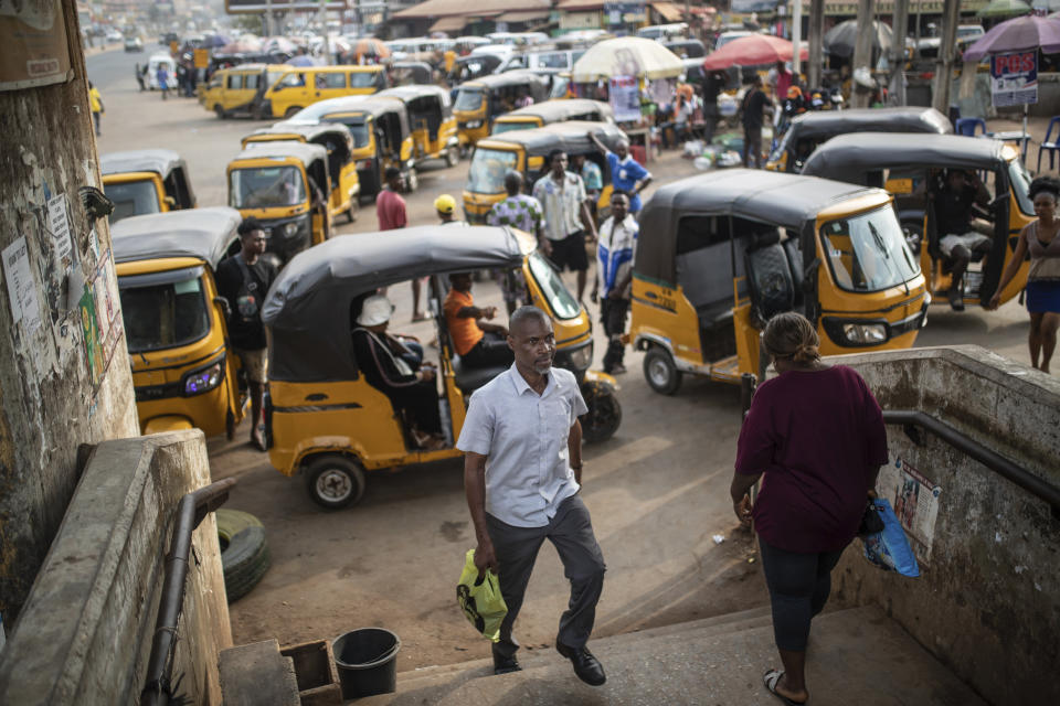 People cross a pedestrian bridge as tricycle drivers wait for customers, in Anambra, Nigeria, Friday, Feb. 24, 2023. Nigerian voters are heading to the polls Saturday to select a new president following the second and final term of incumbent President Muhammadu Buhari. (AP Photo/Mosa'ab Elshamy)