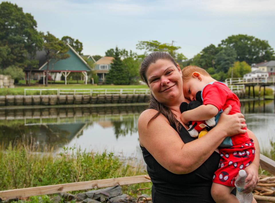 Jenna Goulart holds her son Colton in the backyard of their River Avenue home in Swansea's Ocean Grove neighborhood. Pleasure Island is literally in her backyard, across just over 200 feet of water.