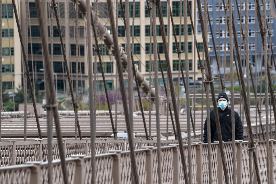 A man wears a facial mask for protection against the coronavirus as he walks over the Brooklyn Bridge, Friday, April 10, 2020, in New York. The new coronavirus causes mild or moderate symptoms for most people, but for some, especially older adults and people with existing health problems, it can cause more severe illness or death. (AP Photo/Mary Altaffer)