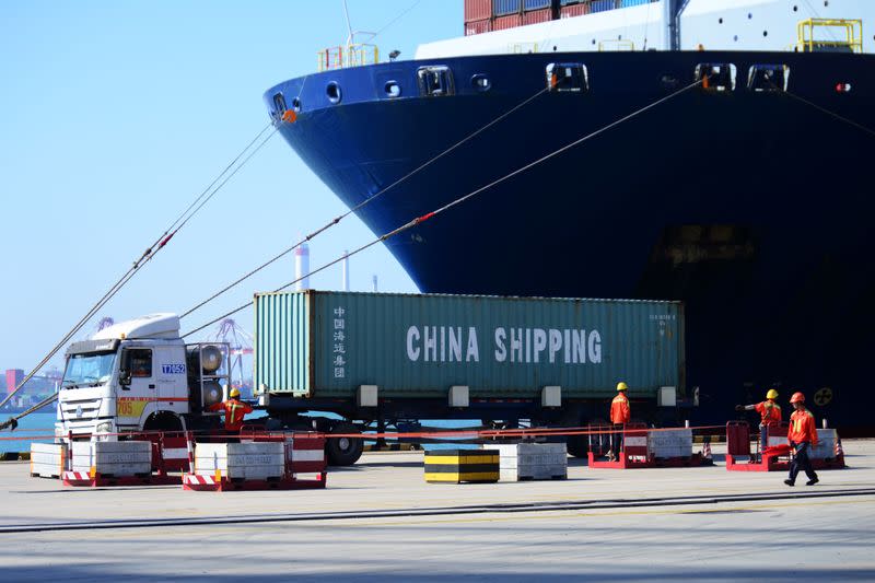 FILE PHOTO: Truck transports a container next to a cargo vessel at a port in Qingdao, Shandong